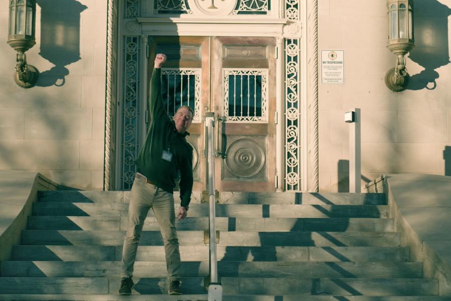 Man (Pete Baier) standing outside of Mesa County Old Courthouse smiling with his fist in the air. 